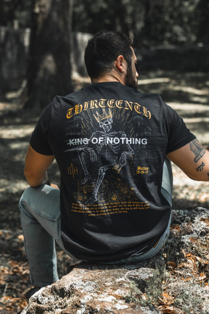 Man sitting on a rock in a forest wearing a black t-shirt with graphic design and text.