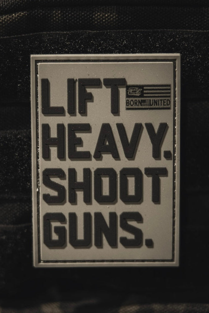 The LHSG - Patch by Tango Charlie Apparel is a rectangular 3D PVC Velcro patch with bold black "LIFT HEAVY. SHOOT GUNS." text, a small American flag, and "BORN UNITED." in the top right corner.