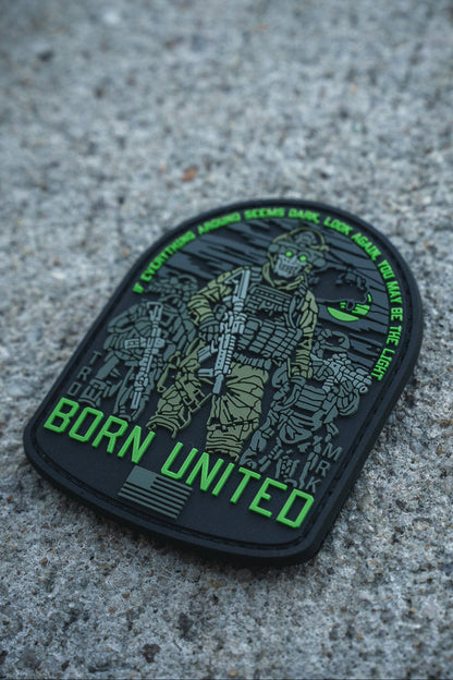 The Light in the Darkness PVC Patch by Born United Private Label features an armed soldier in night vision gear on concrete, "Born United" in bold green, and the quote: “Even if the world seems dark, look for the light. We are the light.”.