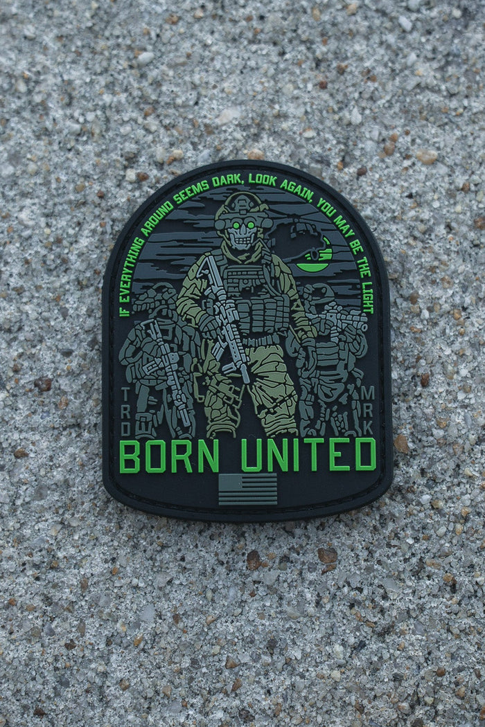 A patch by Born United Private Label, named "Light in the Darkness PVC Patch," features a heavily armed soldier with green accents on rough concrete. The text reads: IF YOU THINK LIGHT SEEMS DARK, LOOK AGAIN. YOU ARE THE LUCK. BORN UNITED below.