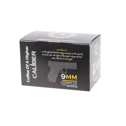 Caliber Coffee Companys black coffee box features Coffee of A Higher Caliber with a gun silhouette. It highlights the 9MM Medium Roasted Complex, nodding to the Second Amendment, and offers medium roast Colombian coffee in single-serve portions.