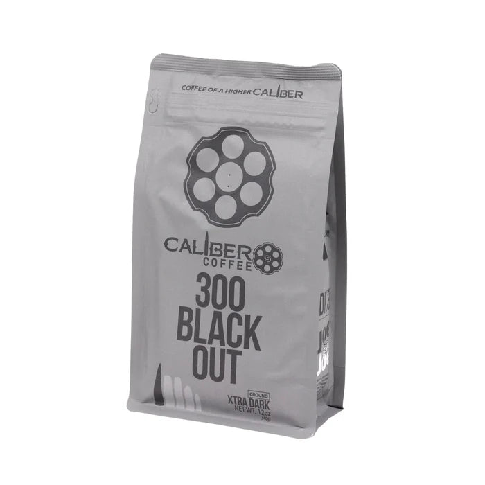 A gray coffee bag with Caliber Dark Roast 300 Blackout - Ground text and a revolver chamber design features Coffee of a higher caliber and Xtra Dark. Made from Specialty Grade, Single Origin South American beans, it stands upright. Brand: Caliber Coffee Company.