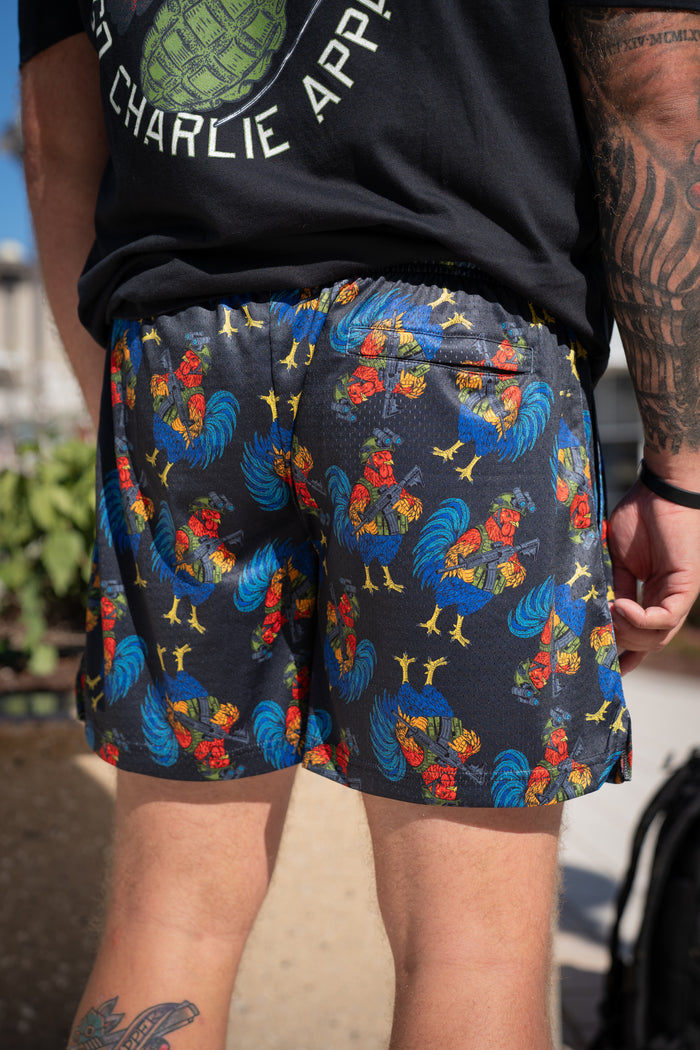 A person outdoors displays only their lower back, legs, and the vibrant Men's Mesh Lifestyle Shorts | 5.5" - Battle Bird by Born United Private Label, highlighting the lively rooster-print design and comfortable fit.