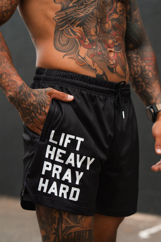 Person wearing black shorts with 'LIFT HEAVY PRAY HARD' text, tattoos visible