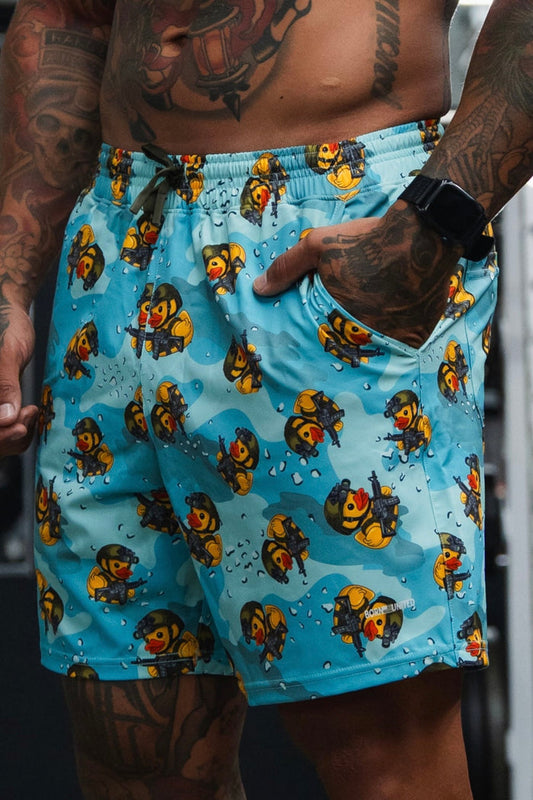 Person wearing blue swim shorts with cartoon character pattern, tattoos visible on arms and chest.