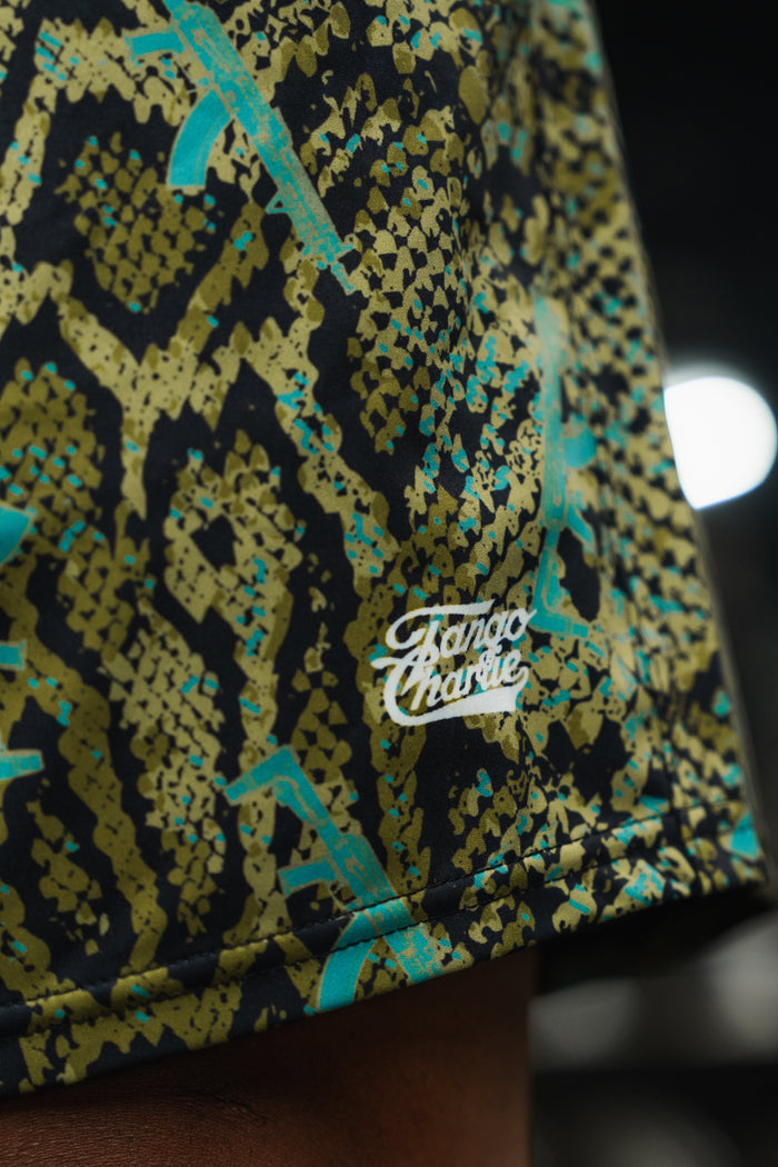 Close-up of green and black snakeskin fabric with blue accents and the white Tango Charlie Apparel logo—featured on Men's Performance Training Shorts | 5.5" - Lethal Venom.