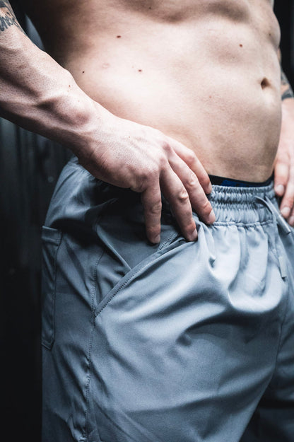 A close-up of a person's bare torso and hand on hip, wearing Born United Private Label Men's Standard Performance Shorts | 5.5" in Gunmetal Gray, with defined muscles visible.