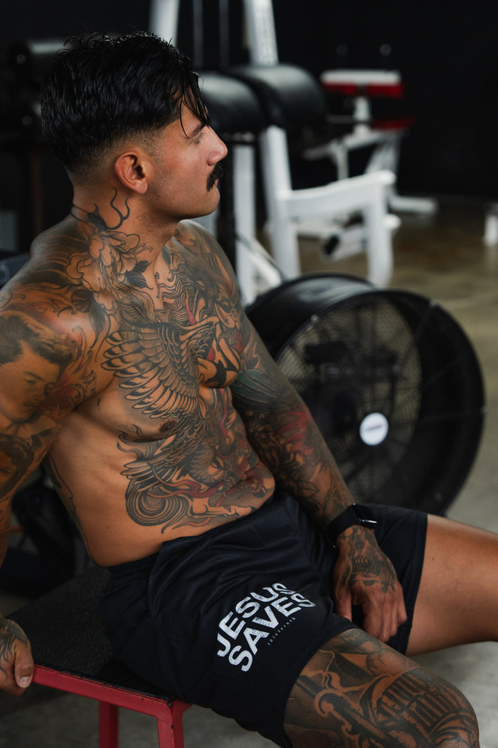 Man with tattoos sitting on a red stool in a gym setting