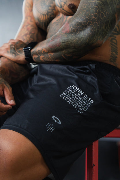 Person sitting on a bench with tattoos and wearing black shorts with text, in a gym setting.