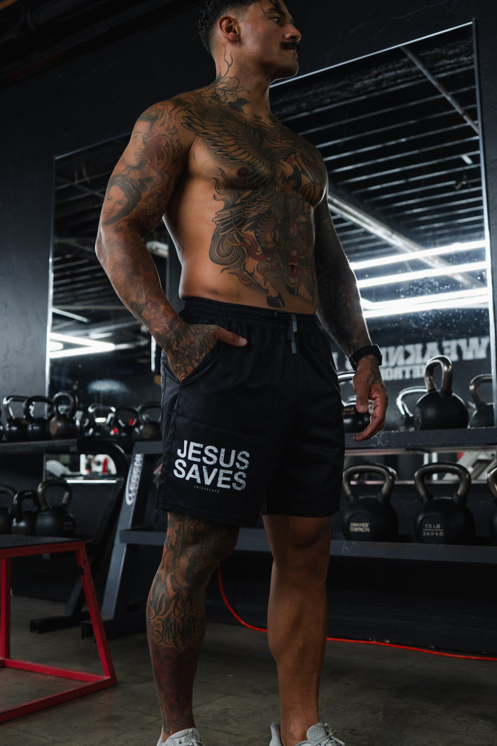 Man in a gym wearing black shorts with 'Jesus Saves' text