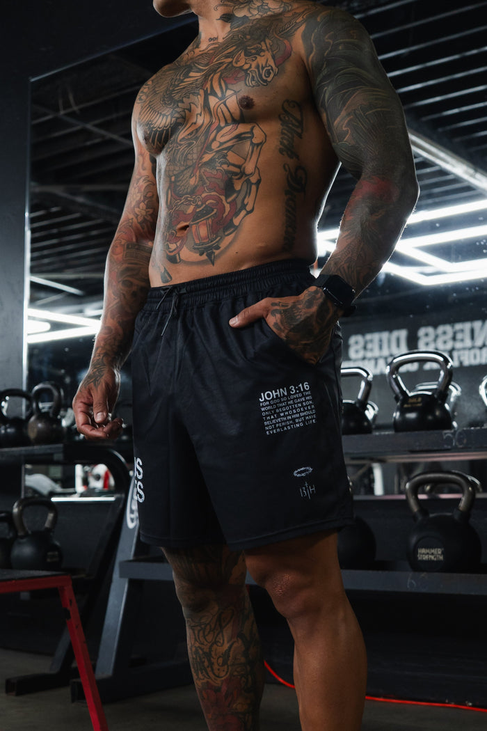 Man with tattoos standing in a gym wearing black shorts.