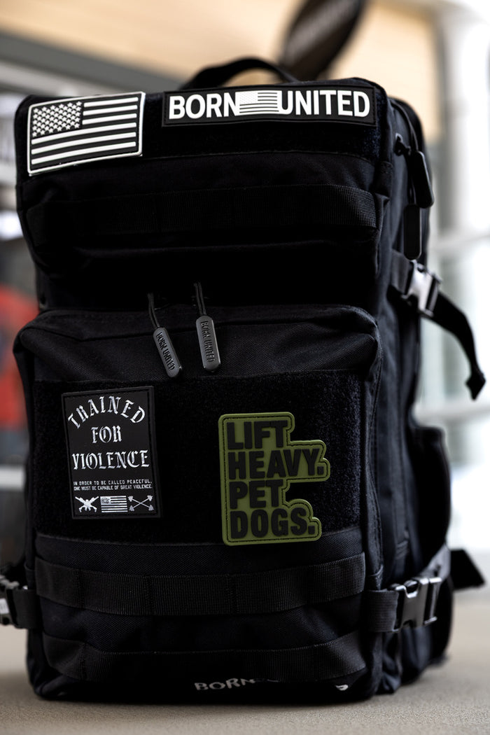 The Born United Private Label Midnight Black Premium Tac-Pac - 45L features patches reading BORN UNITED, an American flag, TRAINED FOR VIOLENCE, and LIFT HEAVY. PET DOGS., plus multi-compartment storage and durable zippers.