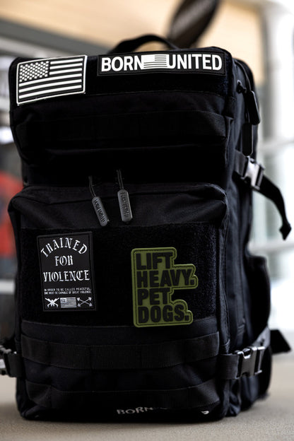 The Born United Private Label Midnight Black Premium Tac-Pac - 45L features patches reading BORN UNITED, an American flag, TRAINED FOR VIOLENCE, and LIFT HEAVY. PET DOGS., plus multi-compartment storage and durable zippers.