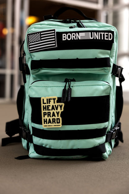 The Mint Condition Tac-Pac - 25L by Born United Private Label is a mint green backpack with black straps and a modular patch panel displaying BORN UNITED, an American flag, and LIFT HEAVY PRAY HARD patches on the front.