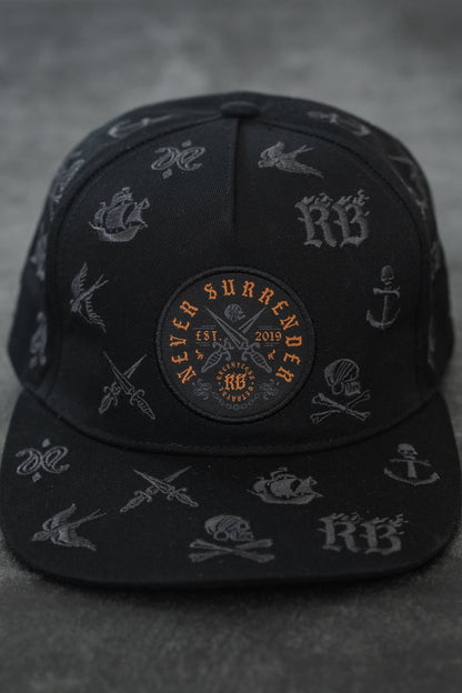 The Never Surrender Limited Edition Snapback by Relentless Betrayal is a black cap with grey nautical and tattoo-style designs, plus an orange and black patch on the front reading "Never Surrender Est. 2019.