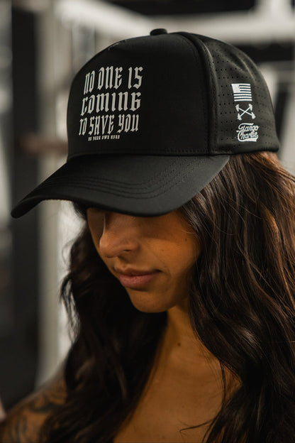 A woman with long dark hair wears the Tango Charlie Apparel No One Is Coming To Save You Hydro - Snapback Hat, featuring white text, a small American flag, and crossed axes design on the side.