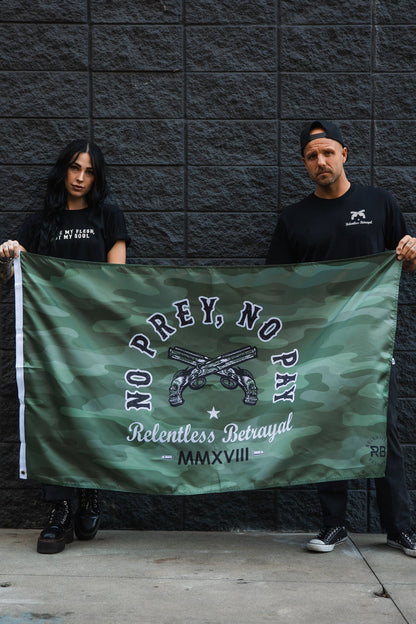 In front of a dark brick wall, two people hold the No Prey, No Pay Camo Flag by Relentless Betrayal, featuring crossed pistols and text about relentless betrayal. Their black attire and serious expressions perfectly match the rebellious spirit of the polyester flag displaying No Prey, No Pay.