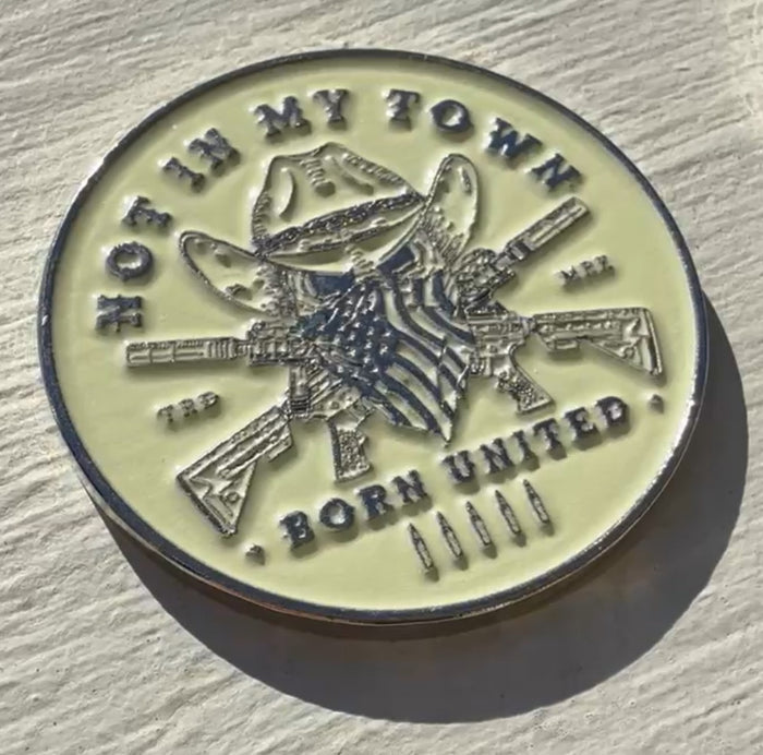 The Not In My Town Challenge Coin by Born United Private Label features a cowboy hat and bandana above crossed rifles and stars. The phrases NOT IN MY TOWN and BORN UNITED arch above and below, with five bullets at the bottom.