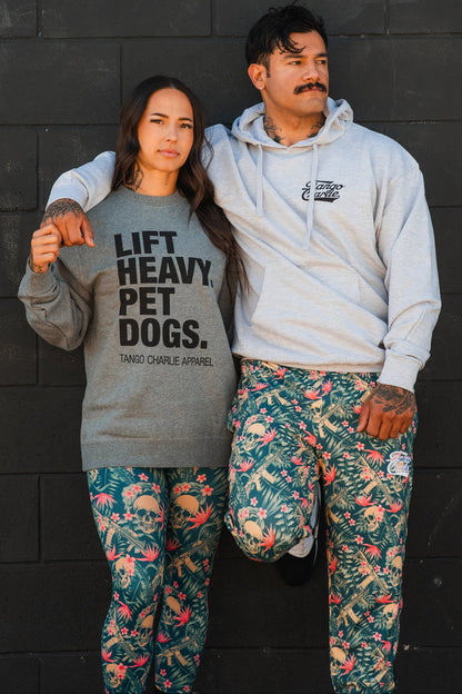 A woman in a gray LIFT HEAVY. PET DOGS. sweatshirt and a man in the Tango Charlie Apparel Only You Can Prevent Dad Bod Hoodie stand confidently against a black wall, both showcasing their gym-inspired looks.