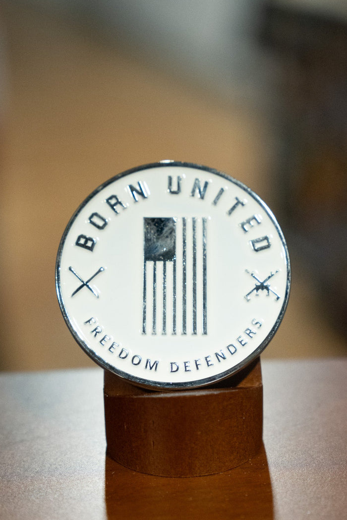 The Outlaw Challenge Coin by Born United Private Label features a round badge with a black and white American flag, “BORN UNITED” above, “FREEDOM DEFENDERS” below, and crossed rifles—perfect for those who protect freedom like outlaws.