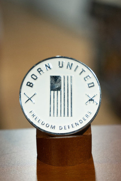 The Outlaw Challenge Coin by Born United Private Label features a round badge with a black and white American flag, “BORN UNITED” above, “FREEDOM DEFENDERS” below, and crossed rifles—perfect for those who protect freedom like outlaws.