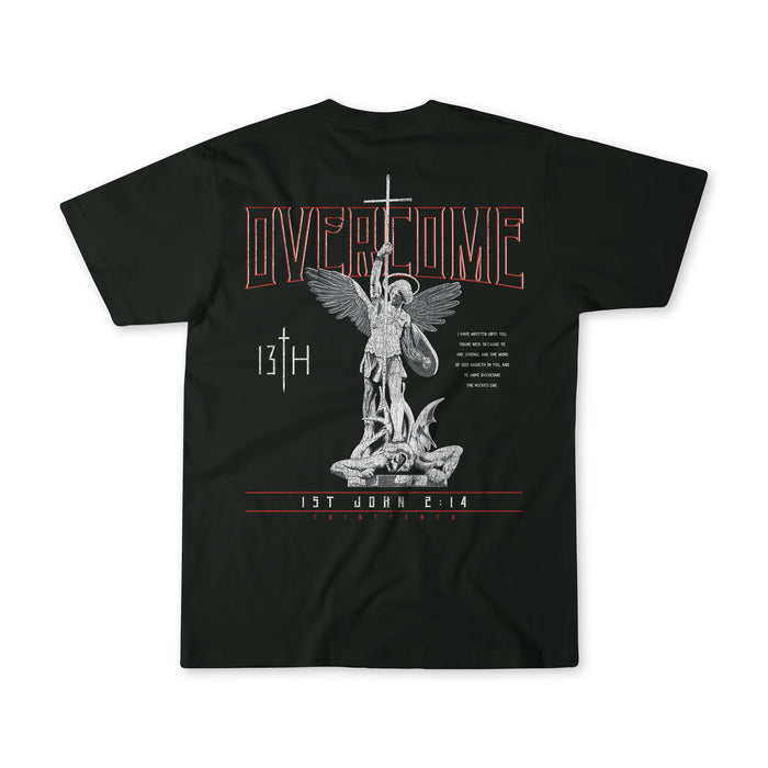 The Overcome Premium Tee by 13th is a black t-shirt with an angel wielding a sword over a creature, featuring the text OVERCOME and 1 John 4:14 to inspire young men with Gods word.