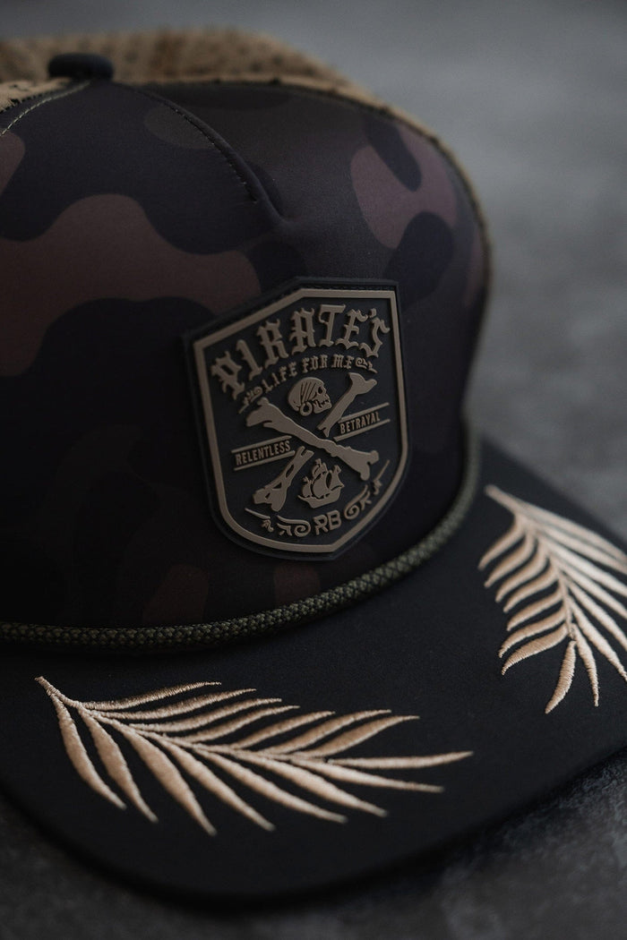 The Pirates Life Camo Snapback by Relentless Betrayal features a patch with Pirates, Life for Me, Relentless, Betrayal and skull and crossed bones flanked by pistols. This water-resistant hat is perfect for adventure seekers with beige embroidered palm leaves on the brim and a green braided trim.