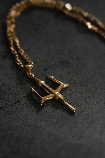 Against a dark, textured backdrop, Relentless Betrayals Poseidons Trident Necklace with its gold, trident-shaped pendant on a matching chain exudes maritime strength and embodies the polished elegance of Greek mythology jewelry.