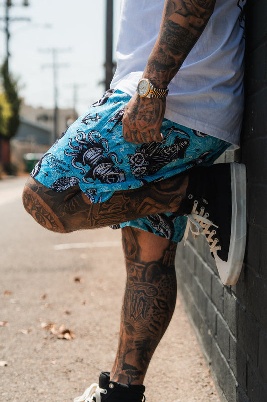Person wearing blue patterned shorts and black sneakers leaning against a brick wall.