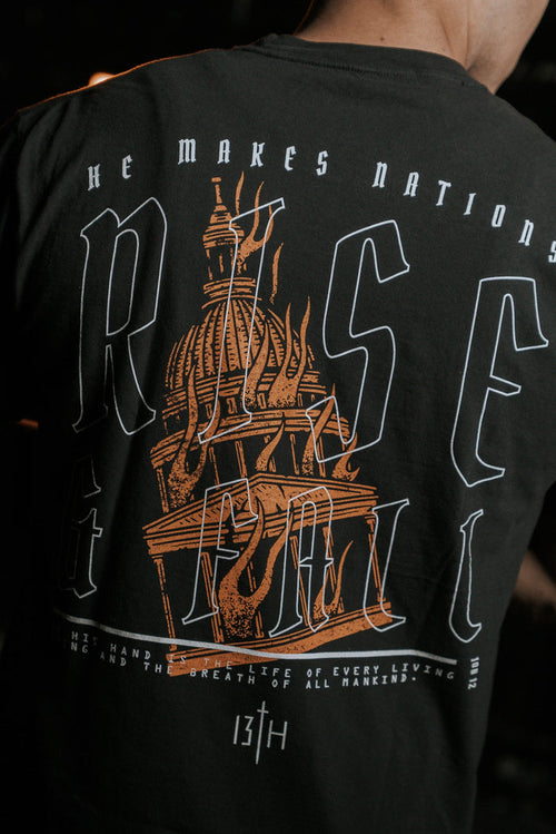 Back view of a person in the black Rise & Fall Premium Tee by 13th, featuring a burning candle inside a dome and the text He makes nations rise & fall and The life of every living thing and the breath of all mankind.
