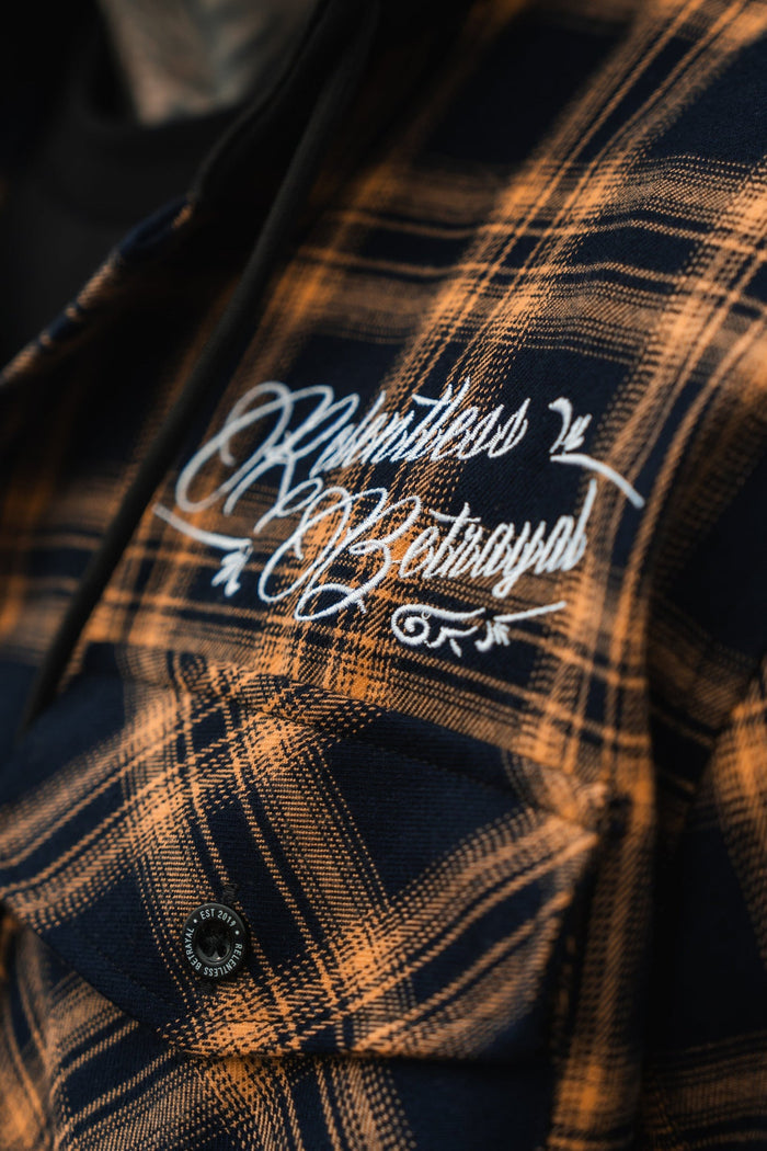 Close-up of someone in a Skilled Sailor Premium Hooded Flannel by Relentless Betrayal, featuring black and yellow plaid. Relentless Betrayal is embroidered in white script on the chest pocket. Made from a cozy cotton/polyester blend, this ultra-soft piece promises comfort and style.