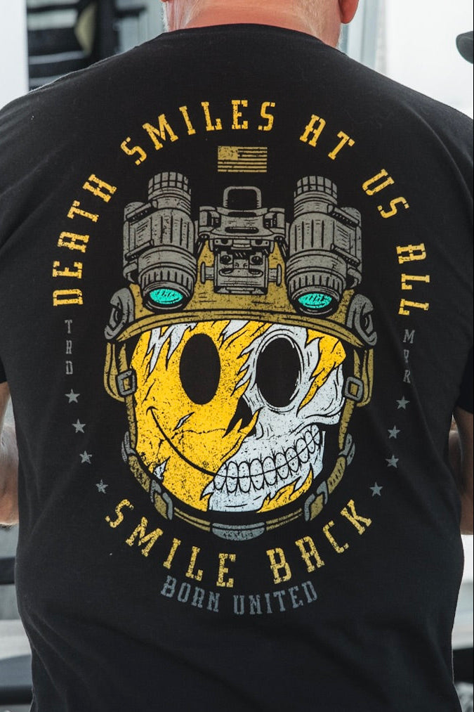 Wearing the Born United Private Label "Smile Back" black tee, featuring a half-skull, half-yellow smiley face in night vision goggles and the message: "Death smiles at us all, smile back." A striking piece of philosophy apparel.