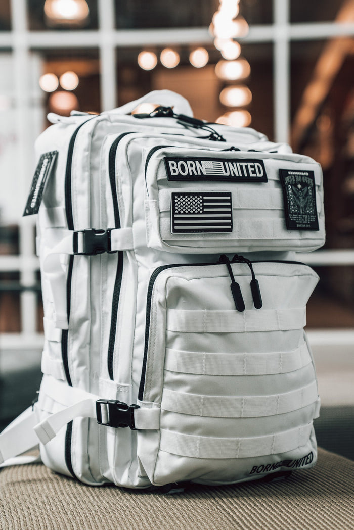 The Standard Tac-Pac Ultimate Bundle by Born United Private Label is a white tactical backpack with black zippers and straps, adorned with patches like “BORN UNITED” and an American flag—perfectly matching any Born United T-shirt.