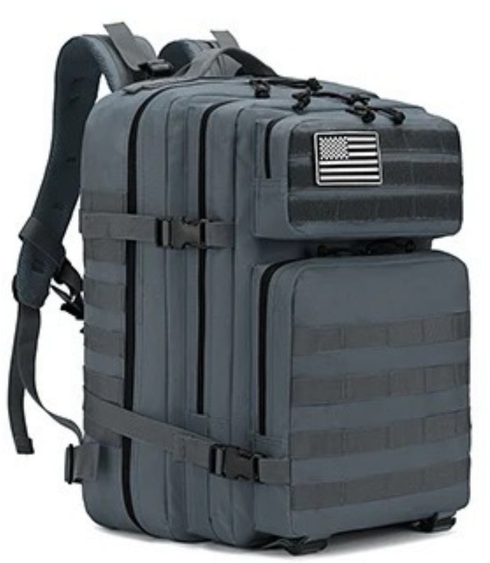 The Born United Private Label Standard Tac-Pac Ultimate Bundle is a dark gray tactical backpack with multiple compartments, front MOLLE webbing, side straps, and an American flag patch—perfectly matching your Born United T-shirt or Hat.