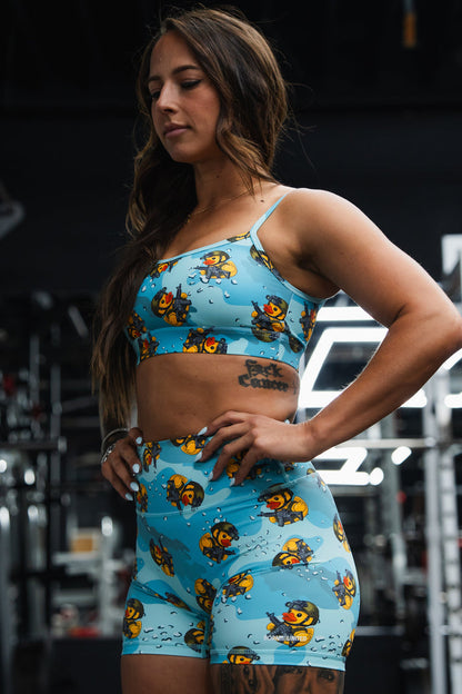A woman stands in a gym, hands on hips and looking focused, wearing Born United Private Label’s Women's High-Waisted Seamless Front Compression Training Shorts | TactiQuack with blue and yellow cartoon duck prints.