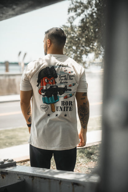 A man stands outdoors with his back to the camera, wearing the Born United Private Label "Sweet Victory" t-shirt, featuring a cartoon popsicle with sunglasses and a gun, plus the phrases “Sweet Treats For All The Haters” and “BORN UNITED.”.