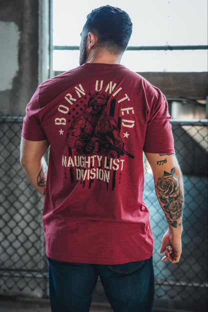 A tattooed man faces away from the camera, wearing the Born United Private Label Tactical Santa Tee—a red limited-edition Christmas shirt featuring an armed Saint Nick and "Naughty List Division." Ideal for fans of standout holiday apparel.