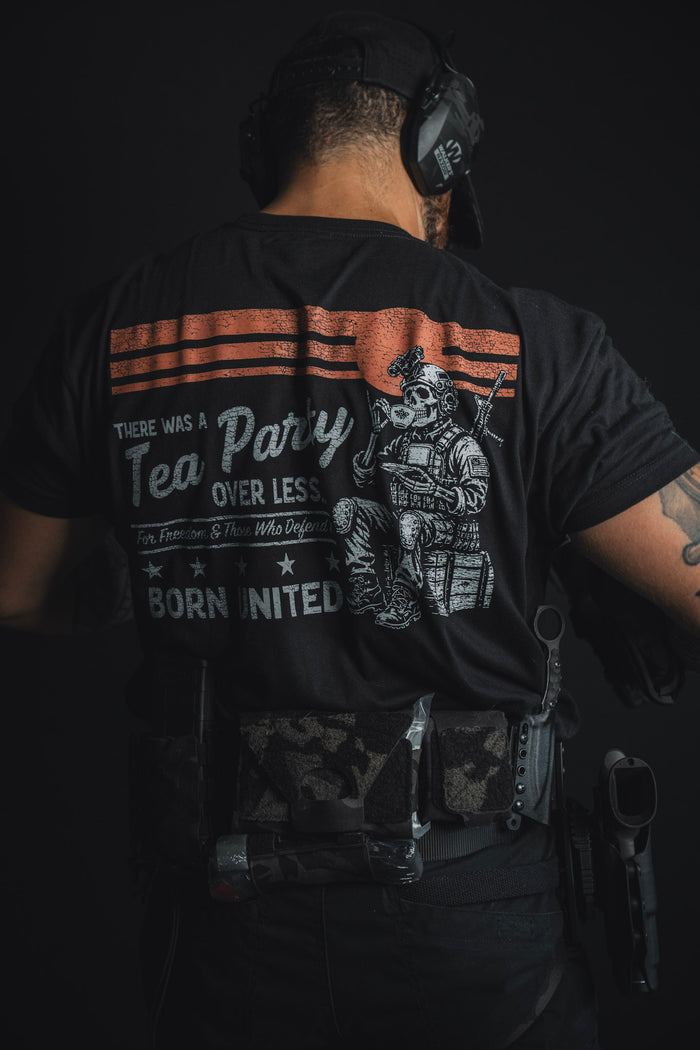 A man dressed in tactical gear and headphones stands with his back to the camera, showcasing the ‘Tea Party’ T-shirt from Born United Private Label, which features the text: “There was a Tea Party over less. Born united.” — a modern nod to historic rebellion.