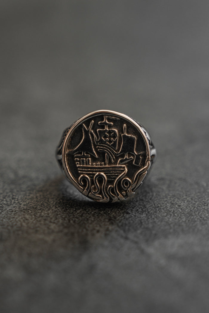 The Rise of the Kraken Ring by Relentless Betrayal, a handcrafted silver ring with intricate geometric and abstract shapes—central triangle, circles, and wavy lines—rests on a smooth, dark surface.