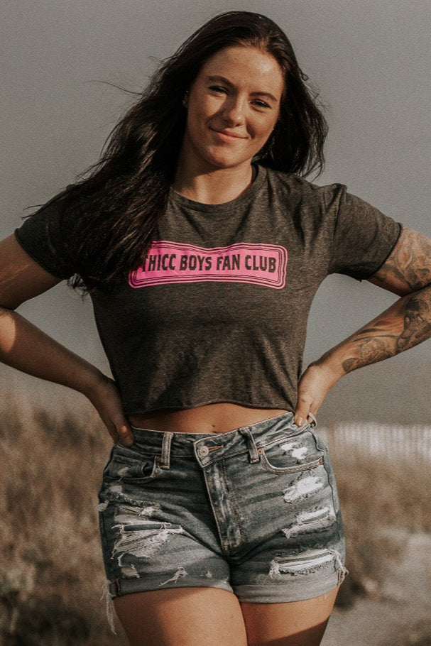 Woman wearing a crop top with 'Hicc Boys Fan Club' text in an outdoor setting