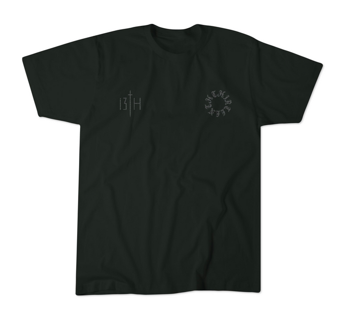 The 13th Victorious Dawn Premium Tee is a black shirt with a small vertical 13TH sword graphic (spiritual strength) on the left chest and a circular cryptic letter design on the right, shown laid flat on a white background.