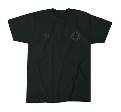 The 13th Victorious Dawn Premium Tee is a black shirt with a small vertical 13TH sword graphic (spiritual strength) on the left chest and a circular cryptic letter design on the right, shown laid flat on a white background.