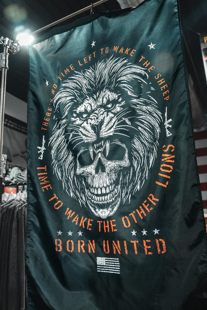 The Waking Lions Flag by Born United Private Label, crafted from durable polyester, shows a roaring lion merged with a skull and reads: "There's no time left to wake the sheep. Time to wake the other lions. Born United." Ideal for indoor display.