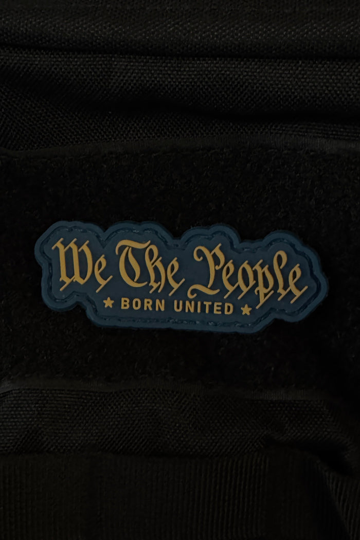 A bold 3-inch “We The People PVC Patch” by Born United Private Label features gold script reading “We The People BORN UNITED” on a dark, star-studded background, and attaches securely to black fabric with Velcro.