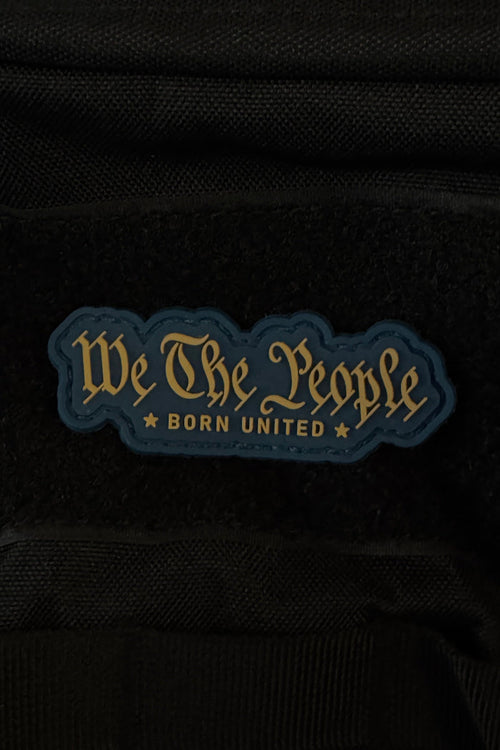 A bold 3-inch “We The People PVC Patch” by Born United Private Label features gold script reading “We The People BORN UNITED” on a dark, star-studded background, and attaches securely to black fabric with Velcro.