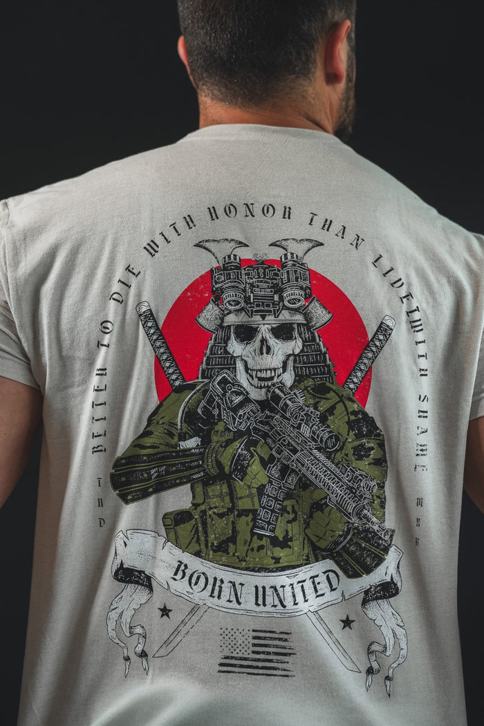 A man wears the "With Honor" T-shirt by Born United Private Label, featuring a skull in samurai armor with a rifle, a red circle backdrop, and the motto "Better to die with honor than live with shame," embodying a modern warrior's spirit.