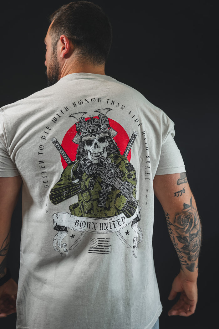 A man faces away, wearing the Born United Private Label "With Honor" T-shirt in light gray, which shows a modern warrior skull in military gear with rifle, red and black accents, and the words "Better to die with honor than live with shame.
