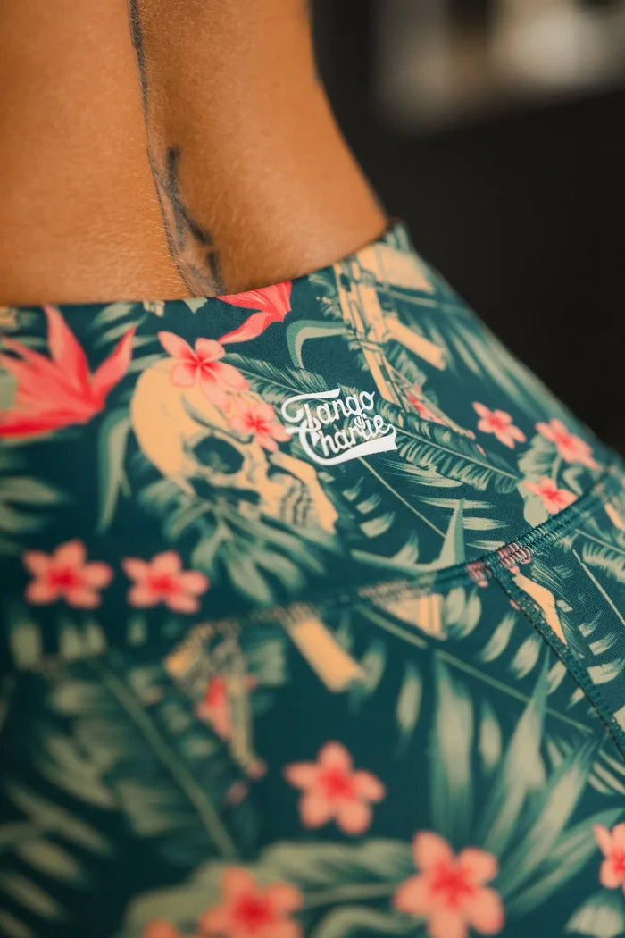 Close-up of a person wearing Tango Charlie Apparel’s Women's Performance Leggings | Aloha AR, featuring a tropical pattern with pink flowers and green leaves. The waistband offers tummy control, and part of a tattoo is visible on the lower back.