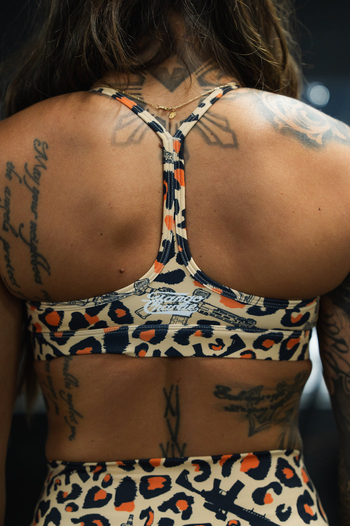 A person with long hair and several tattoos is photographed from behind, wearing the Tango Charlie Apparel Y-Back Sports Bra in Loaded Leopard.